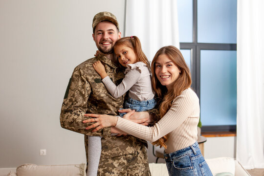 young soldier of the Ukrainian army in a camouflage uniform returned home to his family, a military dad hugs his little daughter and wife at home