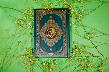 Wall Mural - muslim book with Arabic calligraphy Quran translation :  holy book of Muslims with gypsophila flowers on green background