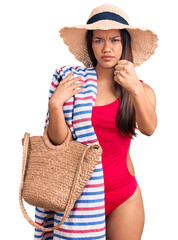 Poster - Young beautiful latin girl wearing swimwear and summer hat holding beach towel and bag annoyed and frustrated shouting with anger, yelling crazy with anger and hand raised