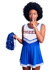 Canvas Print - Young african american woman wearing cheerleader uniform holding pompom asking to be quiet with finger on lips. silence and secret concept.