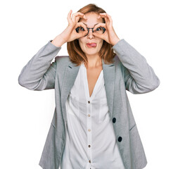 Wall Mural - Young caucasian woman wearing business style and glasses doing ok gesture like binoculars sticking tongue out, eyes looking through fingers. crazy expression.