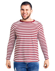 Wall Mural - Young handsome man wearing striped sweater winking looking at the camera with sexy expression, cheerful and happy face.