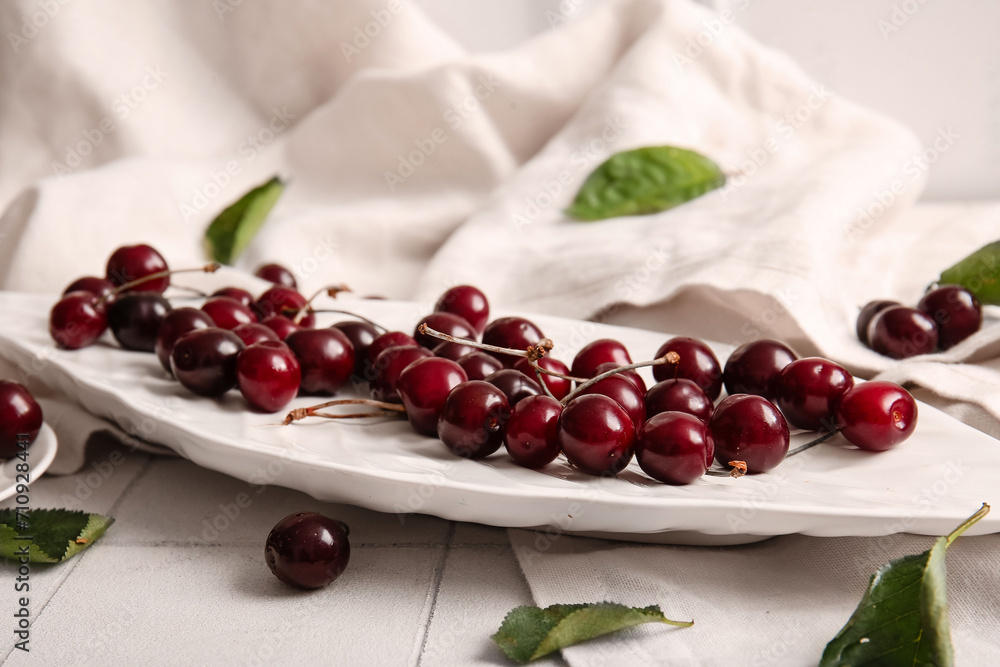 Plate with sweet cherries on white tile table