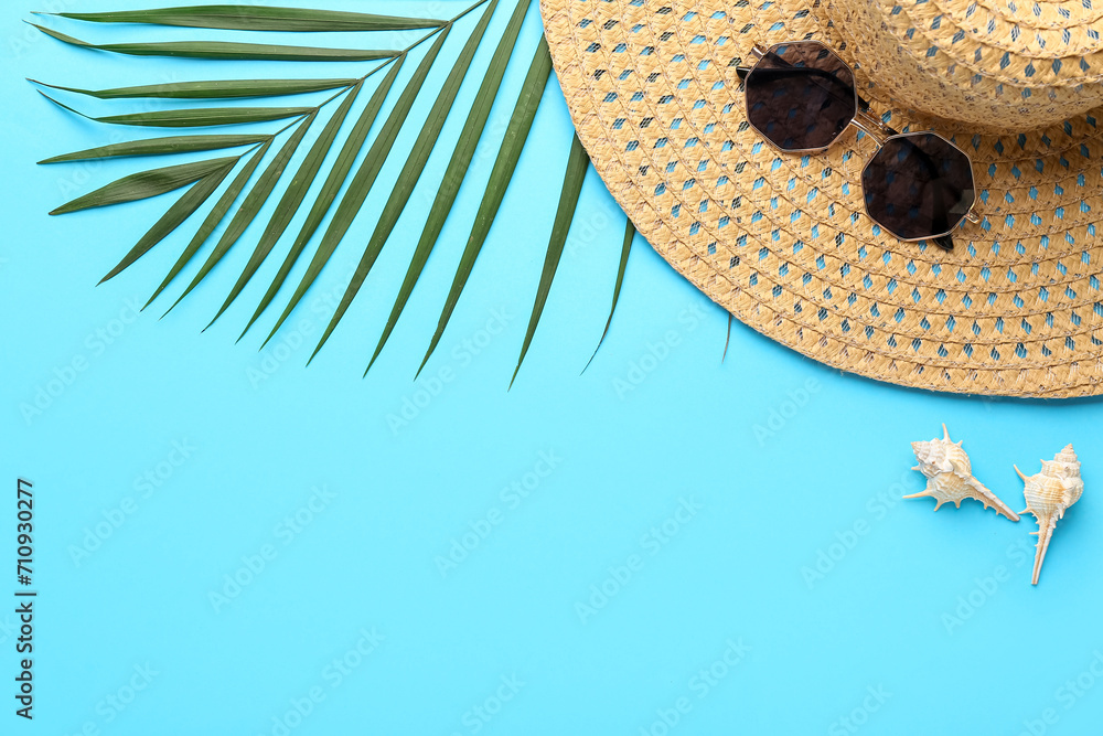 Composition with wicker hat, stylish sunglasses and palm leaf on blue background