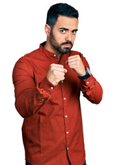 Poster - Young hispanic man with beard wearing casual shirt ready to fight with fist defense gesture, angry and upset face, afraid of problem