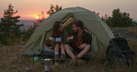 a young man and his girlfriend have dinner and make delicious coffee near a tent in the mountains af