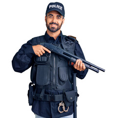 Poster - Young hispanic man wearing police uniform holding shotgun looking positive and happy standing and smiling with a confident smile showing teeth