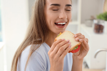 Sticker - Beautiful young woman eating tasty sandwich in kitchen, closeup