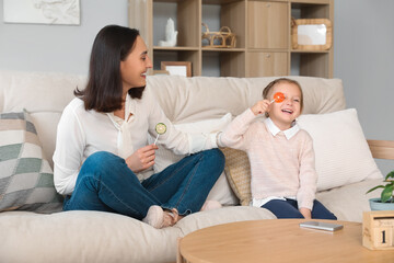 Canvas Print - Beautiful mother and her cute little daughter with sweet lollipops sitting on sofa at home