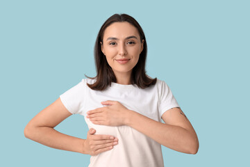 Poster - Young woman checking her breast on blue background. Cancer awareness concept