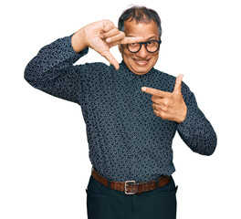 Wall Mural - Middle age indian man wearing casual clothes and glasses smiling making frame with hands and fingers with happy face. creativity and photography concept.