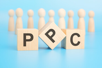 Poster - forming a conceptual word with cubes in the foreground - PPC - Pay Per Click. the cubes are located on a blue surface in front of wooden figures symbolizing people.