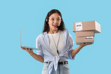 Wall Mural - Young Asian seller in headset with shoe boxes and laptop on blue background