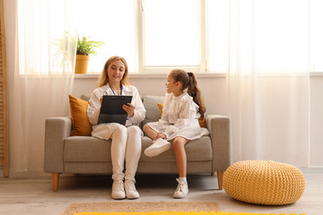 Wall Mural - Mature speech therapist with little girl writing in clipboard in office