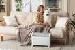 Young woman with plaid and her Samoyed dog on sofa warming near radiator at home