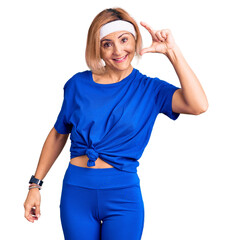 Wall Mural - Young blonde woman wearing sportswear smiling and confident gesturing with hand doing small size sign with fingers looking and the camera. measure concept.