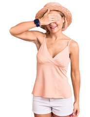 Poster - Young blonde woman wearing summer hat smiling and laughing with hand on face covering eyes for surprise. blind concept.