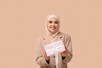 Sticker - Happy young Muslim woman in hijab with gift box on beige background