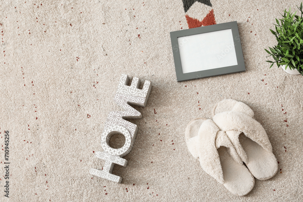 Soft slippers with blank frame, houseplant and word HOME on carpet
