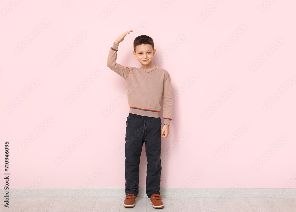 Cute little boy measuring height near pink wall