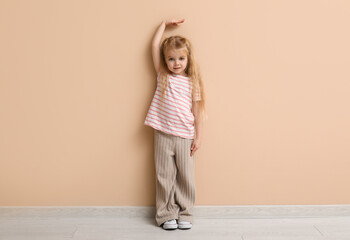 Wall Mural - Cute little girl measuring height near beige wall