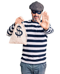 Sticker - Middle age handsome man wearing burglar mask holding money bag with open hand doing stop sign with serious and confident expression, defense gesture