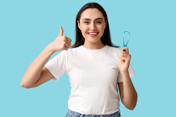 Poster - Young woman with tongue scraper showing thumb-up on blue background