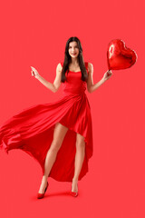 Poster - Beautiful young woman with heart-shaped air balloon on red background. Valentine's day celebration