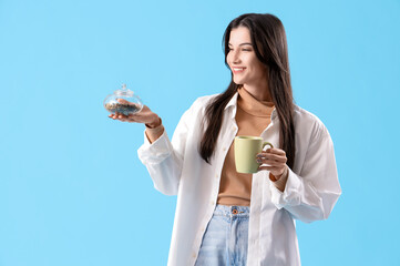 Poster - Beautiful young woman with dry tea and cup of hot beverage on blue background