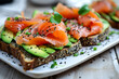 Healthy and gourmet open-faced sandwich with ripe avocado slices and smoked salmon, sprinkled with black sesame seeds and fresh greens