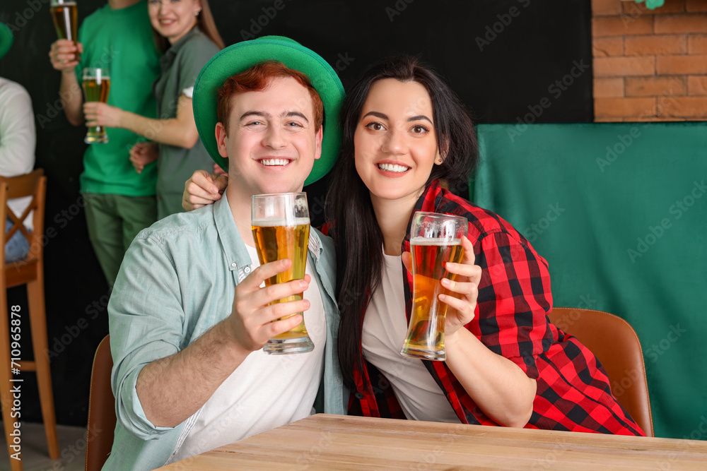 Young couple with beer celebrating St. Patrick's Day at table in pub