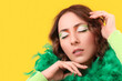 Woman with festive Irish makeup and feather boa on yellow background. St. Patrick's Day celebration
