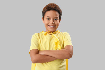 Wall Mural - Cute little African-American boy in superhero costume with yellow ribbon on grey background. Childhood cancer awareness concept