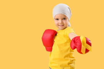 Wall Mural - Cute little girl in boxing gloves with yellow ribbon on color background. Childhood cancer awareness concept