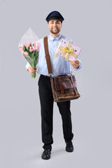 Wall Mural - Handsome postman with tulips and gift box on light background. International Women's Day celebration