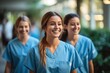© duyina1990 - Three smiling female nurses in blue scrubs walk down a hospital hallway