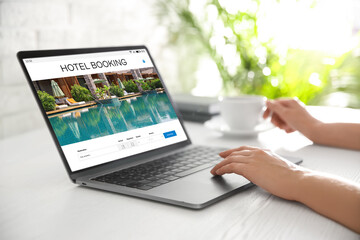 Woman using laptop to book hotel at white wooden table, closeup