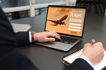 Wall Mural - Man using laptop to book flight at black table, closeup