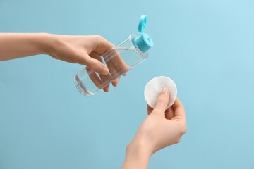 Wall Mural - Woman pouring makeup remover onto cotton pad on light blue background, closeup