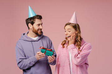 Happy emotional couple of friends celebration birthday isolated on pink background. Smiling man giving gift box for beautiful excited woman. Holiday, Party concept  