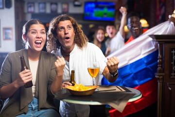 Poster - Excited diverse soccer supporters with flag of Russia watching tournament with pint of beer and chips in the pub