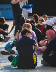 Wall Mural - Group of tourists sitting during outdoor excursion tour in the city streets with guide, a docent with a tourist adult visitors, school college field trip, students urban tour in a summer sunny day