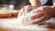 Closeup of a persons hands kneading a ball of homemade dough on a floured countertop.