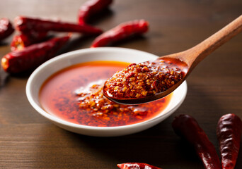 An edible chili oil in a ceramic dish placed on a wooden background. Scooped up with a wooden spoon. Close-up.