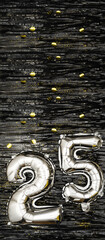 Wall Mural - Silver foil balloon number 25 on a background of black tinsel decoration with golden confetti. Birthday greeting card, inscription twenty-five. Anniversary event. Vertical Banner.