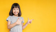 Portrait of young fun smart happy little cute asian girl isolated on yellow background with copy space studio shot. Education for elementary kindergarten, little girl point up back to school concept