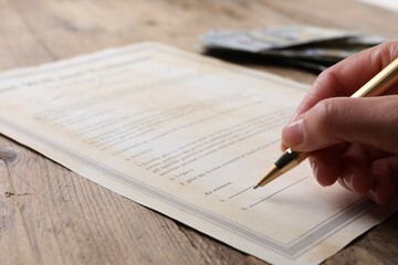 Wall Mural - Woman signing Last Will and Testament at wooden table, closeup