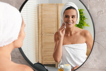 Poster - Young woman cleaning her face with cotton pad near mirror in bathroom