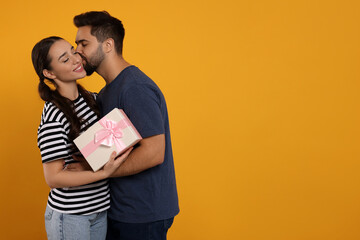 Poster - Man kissing his smiling girlfriend on orange background, space for text. Celebrating holiday