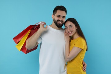 Wall Mural - Happy couple with shopping bags on light blue background